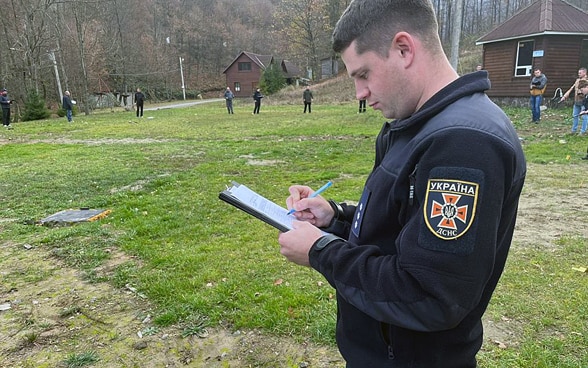 Un uomo, in piedi in un prato, prende appunti su un foglio.