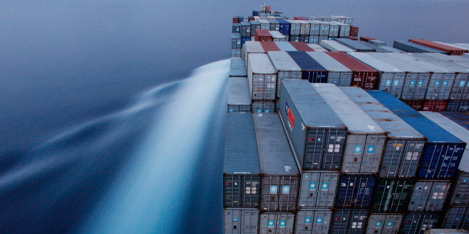 A boat carries piles of containers. Water in the background.