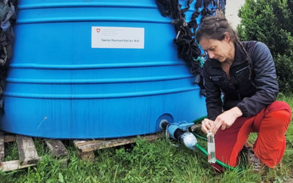 Una donna si inginocchia accanto a un serbatoio d'acqua e lascia scorrere l'acqua in una bottiglia.