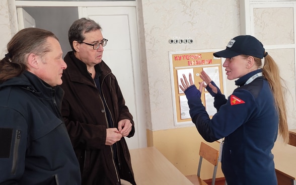 Una donna con l’uniforme della FSD spiega il suo lavoro al direttore della fondazione e a un altro membro dello staff.