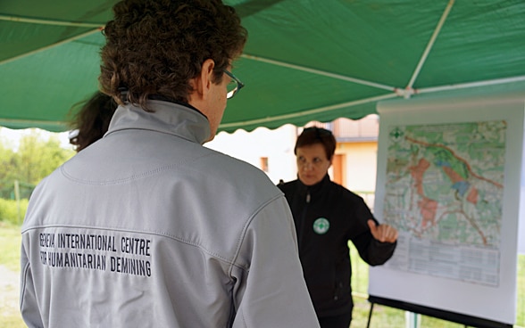 Un uomo di spalle indossa una giacca con la scritta CIDHG e guarda una donna che sta spiegando le cose su una mappa.