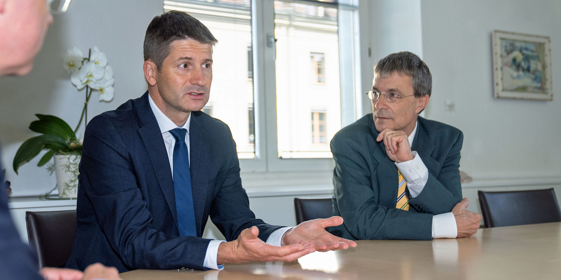 Gabriel Lüchinger parla seduto a un tavolo. Franz Perrez siede alla sua destra e lo ascolta.