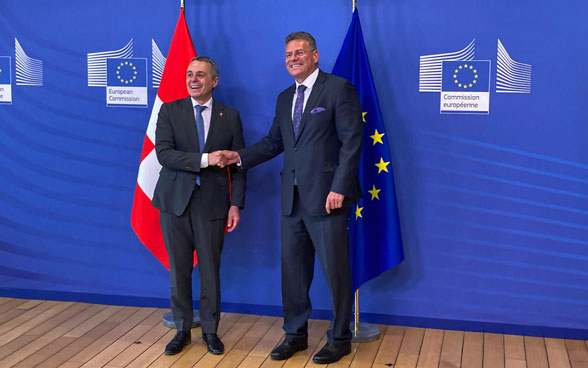 Ignazio Cassis and Maroš Šefčovič shake hands. The Swiss and European flags are in the background.