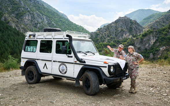 Un soldat et une soldate de l'armée suisse au sein de la KFOR discutent à côté d'un véhicule d'intervention blanc au Kosovo.