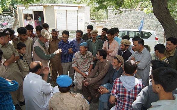 Un observateur militaire suisse est assis au milieu d'une foule de personnes dans un village de la région du Cachemire et écoute leurs explications.