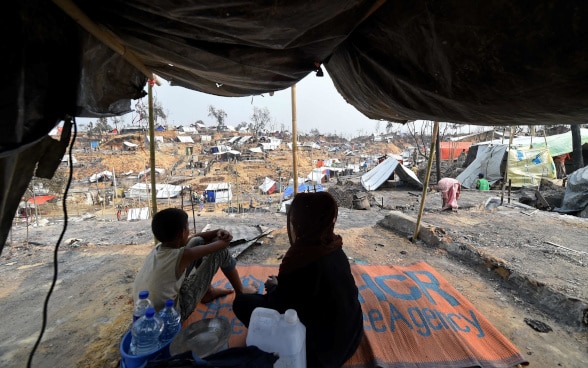 Una donna e un bambino sullo sfondo dei rifugi di fortuna allestiti per gli sfollati Rohingya.