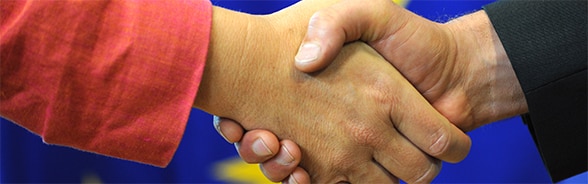 Foto di una stretta di mano con la bandiera europea sullo sfondo