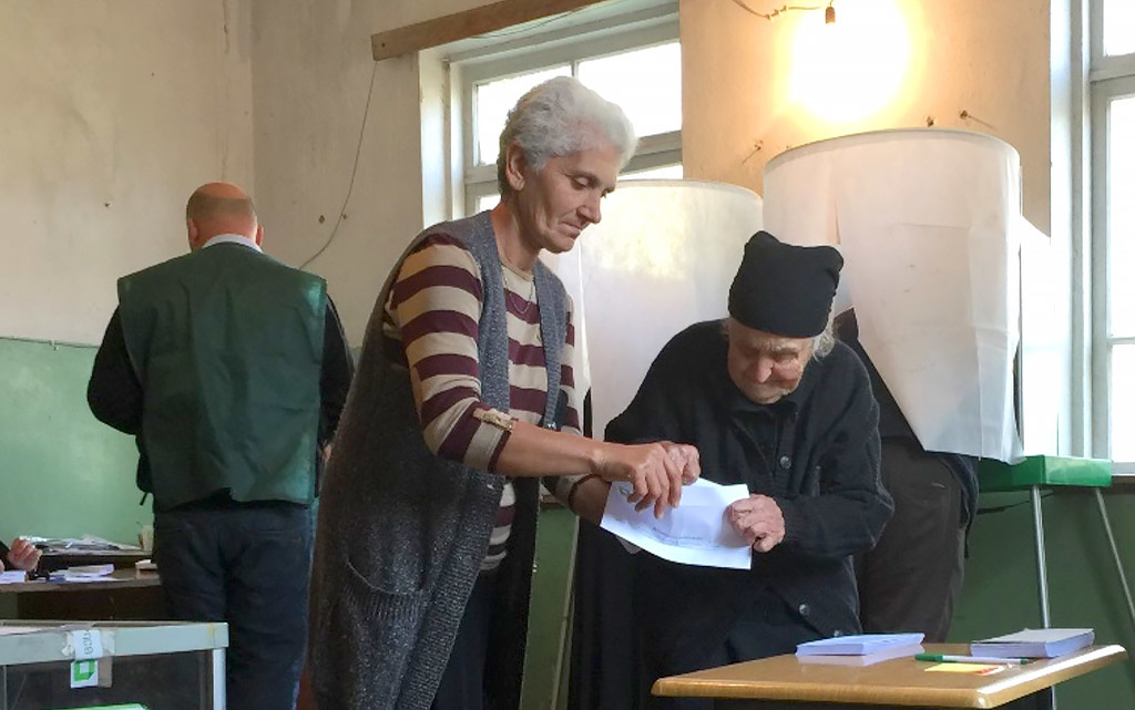 Two women in front of a ballot box during local elections in Georgia. One helps the other to fold a ballot paper at a polling station.