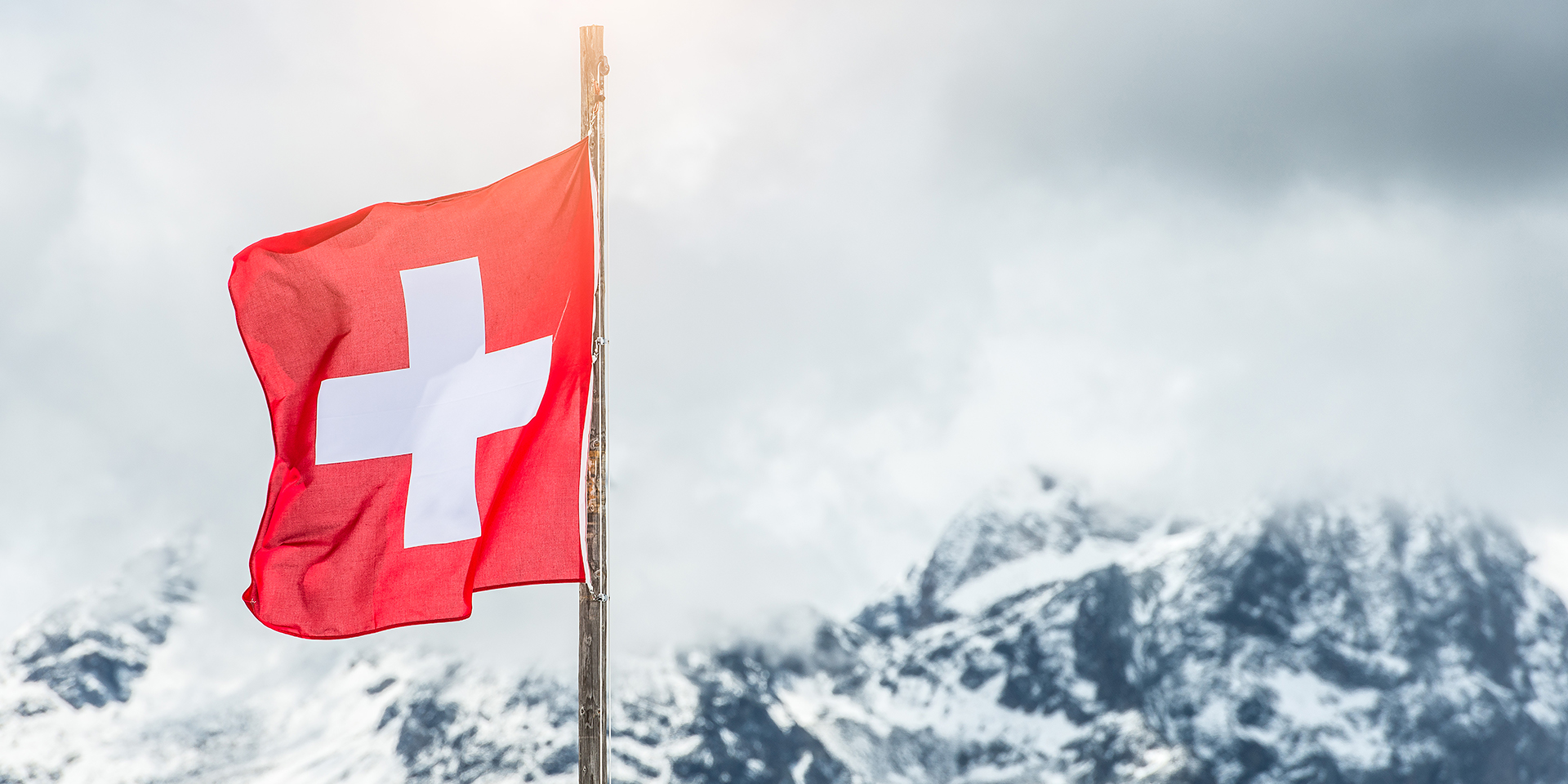 Swiss flag in front of mountains.