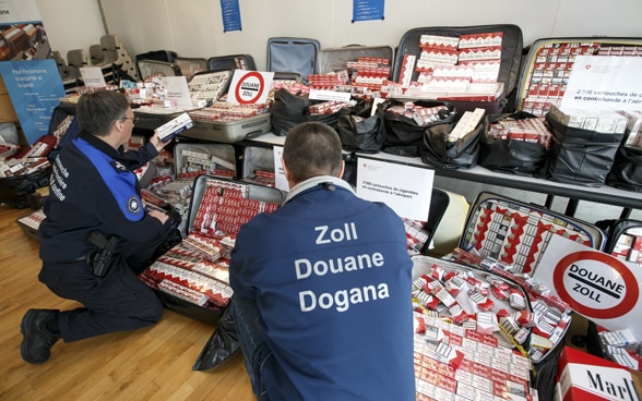 Un garde-frontière et un douanier présentent 3500 cartouches de cigarettes après une saisie douanière à l'aéroport de Genève.