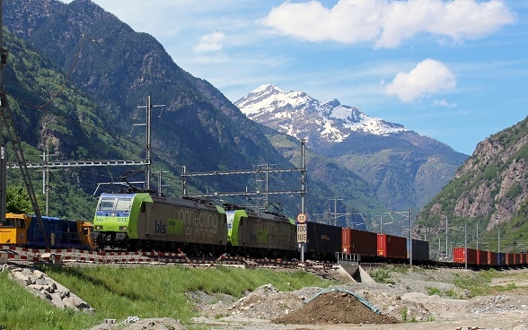 Treno merci con container in un paesaggio alpino.