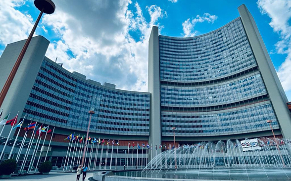  Un bâtiment moderne de plusieurs étages avec des drapeaux de différentes nations et une fontaine devant.