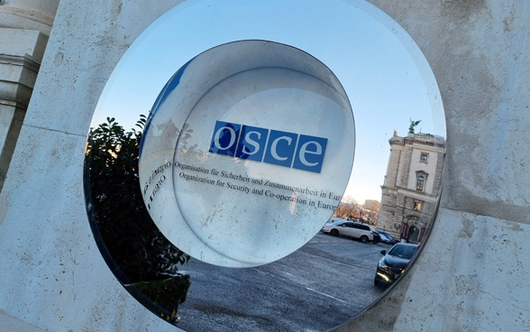 Das Logo der OSZE an einer Hausmauer hinter Glas.