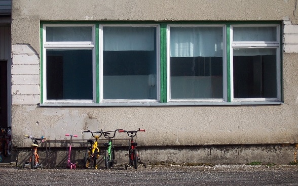 Quattro biciclette davanti a una scuola. La facciata, grigia e sgretolata, è solo invetriata.