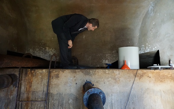 Debout sur un mur, un homme se penche pour regarder au fond d’un réservoir d’eau potable.