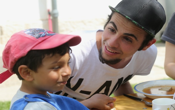 A young man and a boy eating together in the PeCA children's home. 