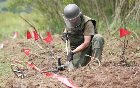 Ein Mann in Schutzkleidung bei der Entschärfung einer Mine auf einem Feld.