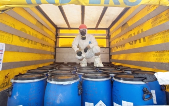 Homme en combinaison de protection dans un camion transportant des fûts remplis de pesticides. 