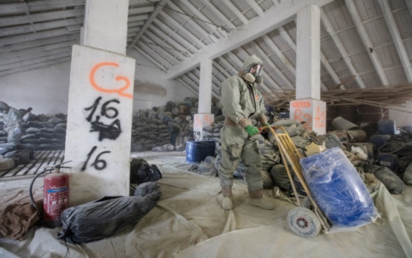 Man in protective clothing pushes a container through a dilapidated warehouse