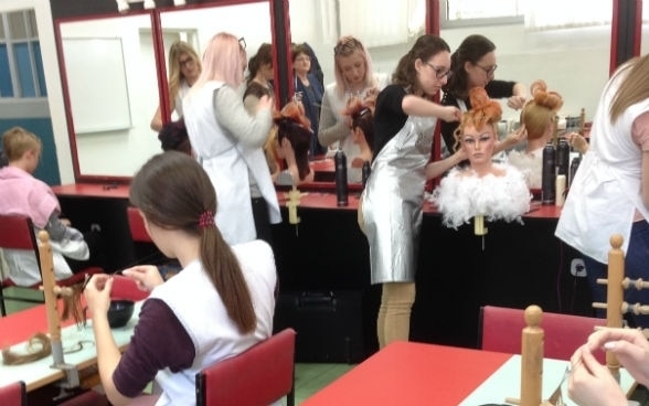De jeunes femmes s’exercent sur des mannequins dans un salon de coiffure.