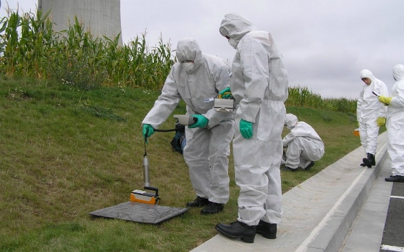Mitarbeitende in weissen Schutzanzügen messen radioaktive Strahlung.