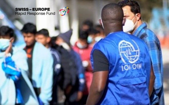 A cultural mediator from IOM is in conversation with a migrant to support him. Other migrants can be seen in the background.
