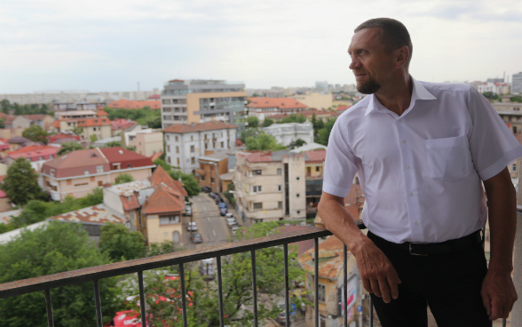 Francisc Giurgiu, Romanian chair of the Opération Villages Roumains - Suisse, standing on a balcony.