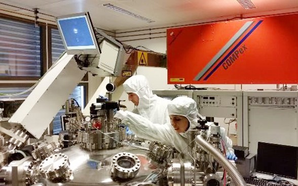 Two researchers in protective suits working on a machine.
