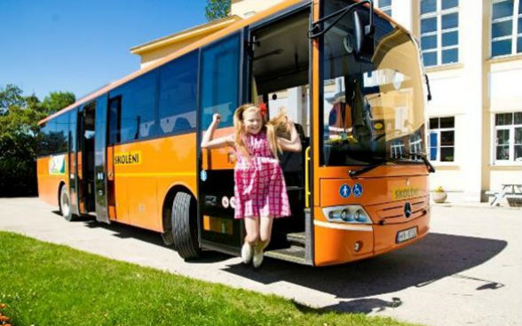 A young girl jumps for joy in front of a school bus.