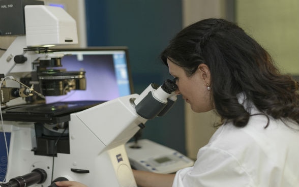 A woman working in a laboratory at a microscope.