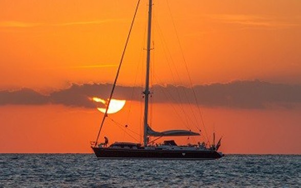 Un yacht navigue en haute mer au soleil couchant.