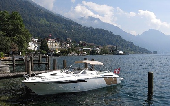 Un bateau à moteur blanc est amarré à un ponton,devant un paysage de montagne.